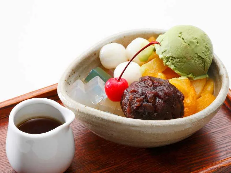 Bát kem trái cây nhiều màu đặt cạnh bình trà trên bàn gỗ