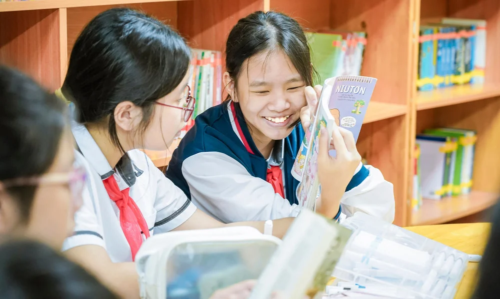 Hai nữ sinh cấp 2 cười tươi đọc sách trong thư viện trường học