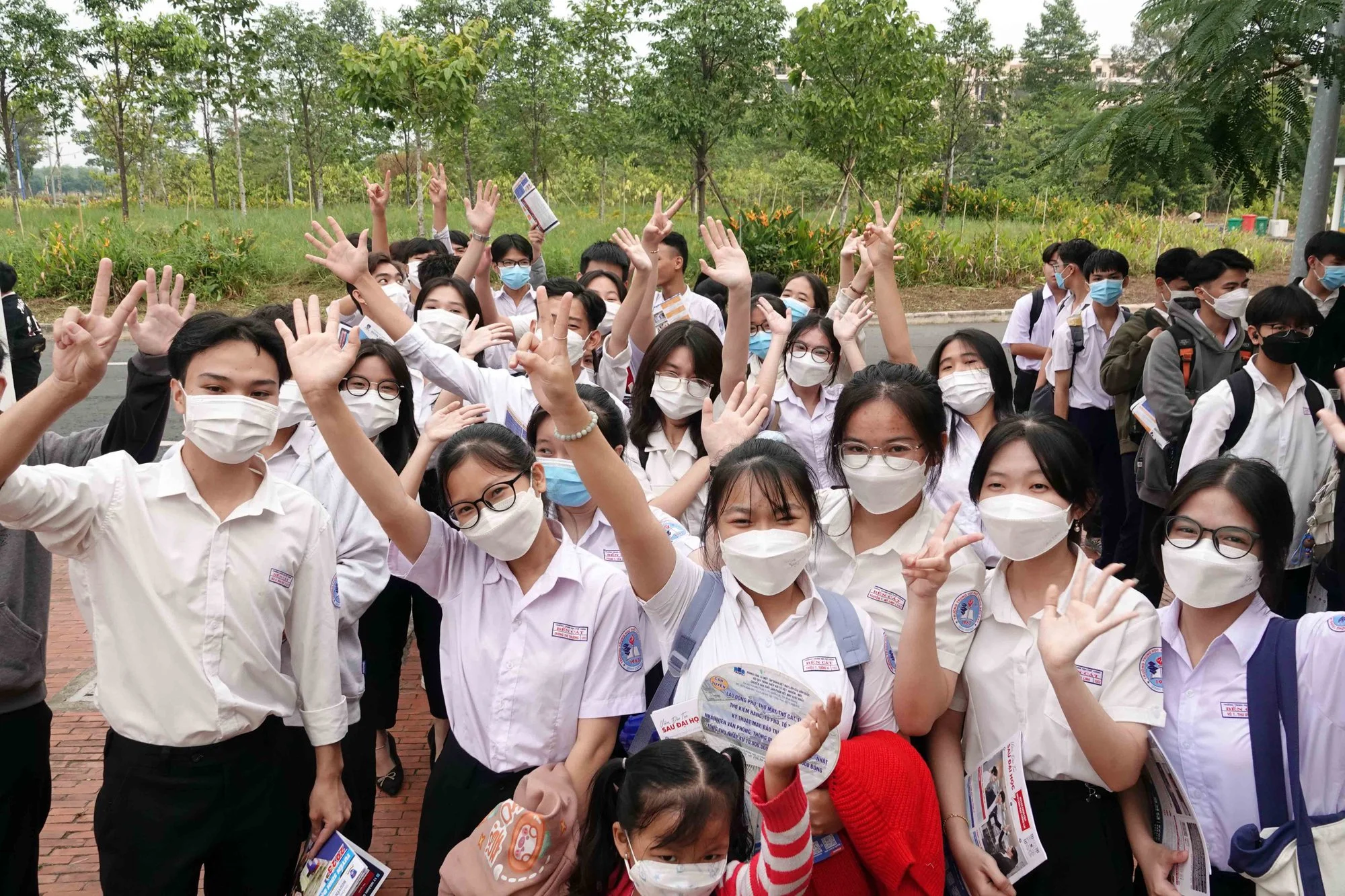Nhóm học sinh cấp 2 mặc đồng phục đeo khẩu trang vẫy tay chụp ảnh tập thể ngoài trời